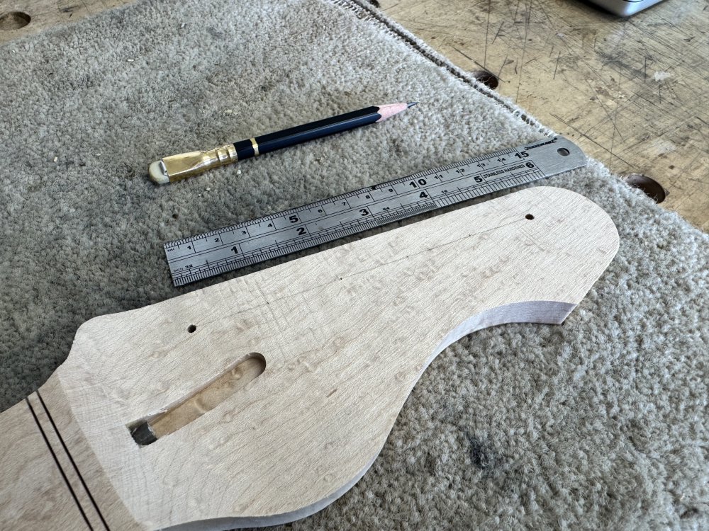 A photo of the blank headstock face on the work-in-progress guitar neck. There are two small drill holes visible where the outer two tuners should go, and a pencil drawn line connecting them, with tick marks to indicate where the other four holes should go.