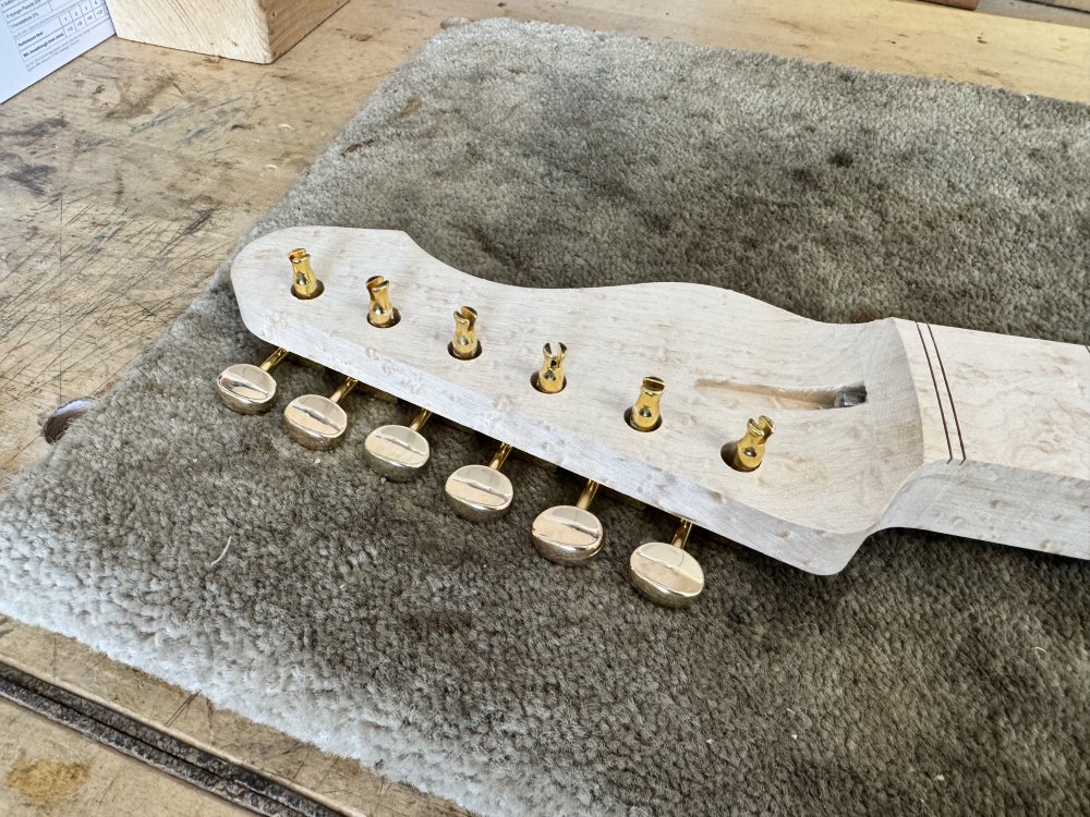A photo of the headstock again, but now it has 6 large holes in it, into which the tuners have been loosely placed.
