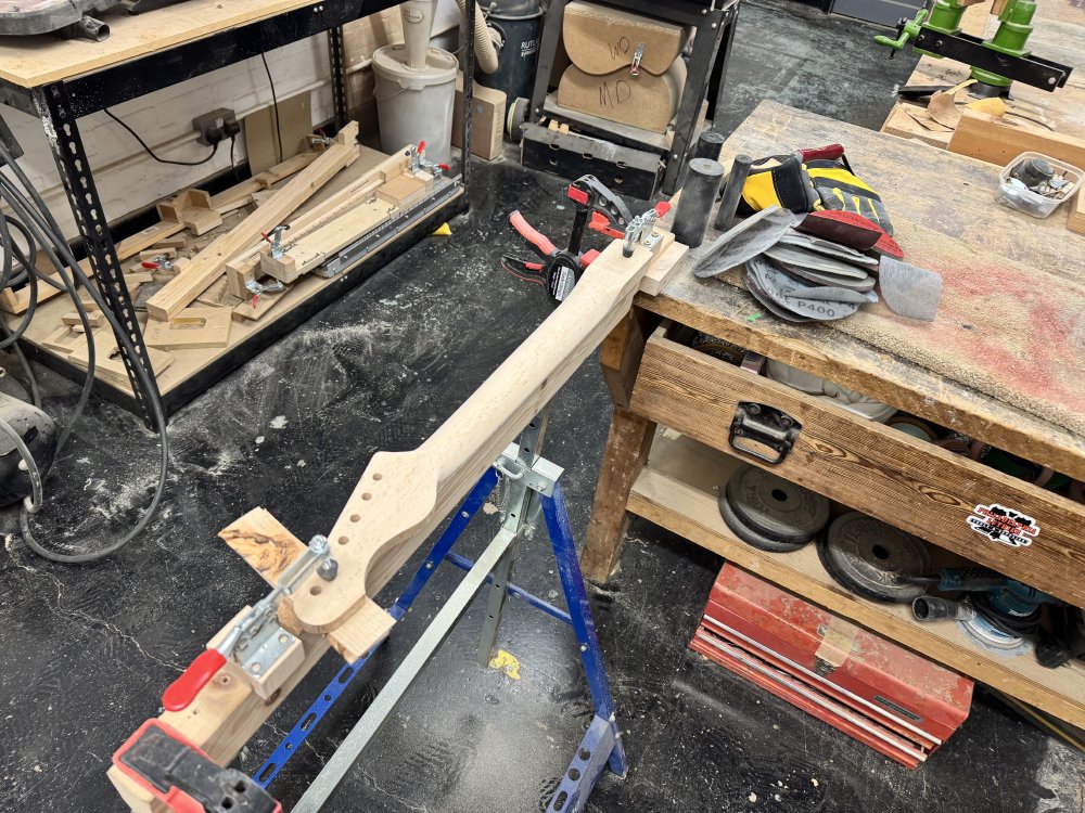Another photo of the guitar neck clamped into the trestle, but now it is much smoother and more rounded looking close to being finished.